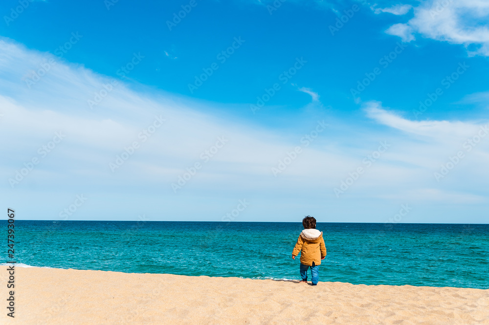 lonely baby boy walking alone on sand beach during sunny day going away