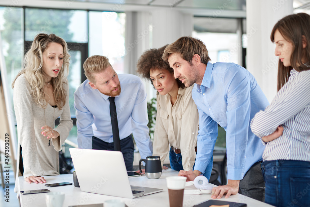 Fototapeta premium Small group of business people standing in office, looking at laptop and developing business plan. Start up business concept.