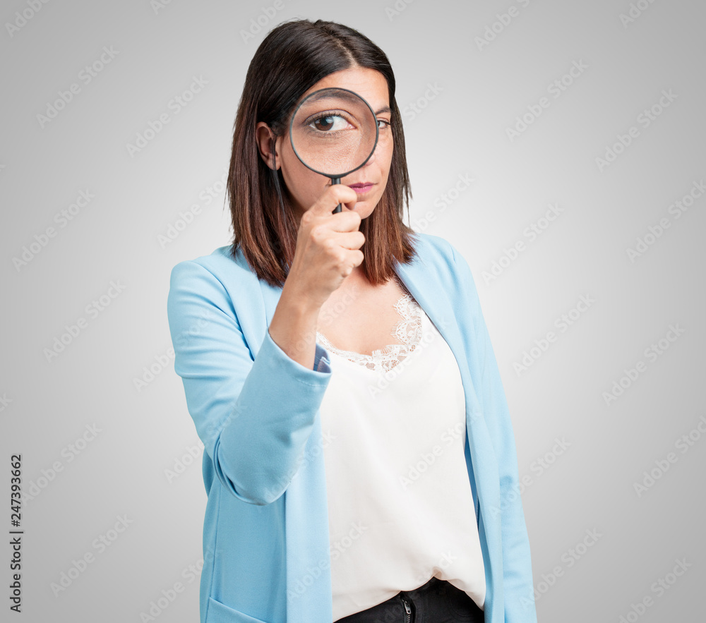 Middle aged woman surprised and wide-eyed looking through a magnifying glass, studying something, finding evidence Middle aged woman surprised and wide-eyed looking through a magnifying glass, studying something, finding evidence
