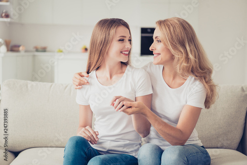 Close up photo of two people pretty excited mum mommy and teen daughter hands arms together look to eyes cute sweet gladly smiling wear white t-shirts jeans sit on comfy sofa