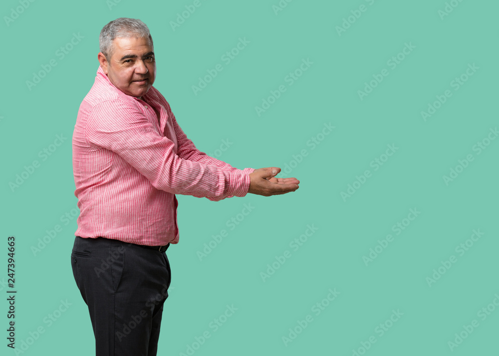 Middle aged man holding something with hands, showing a product, smiling and cheerful, offering an imaginary object Middle aged man holding something with hands, showing a product, smiling and cheerful, offering an imaginary object