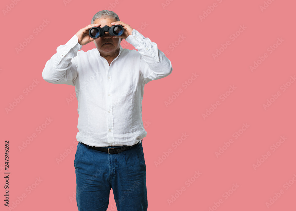Middle aged man surprised and amazed, looking with binoculars in the distance something interesting, concept of future opportunity Middle aged man surprised and amazed, looking with binoculars in the distance something interesting, concept of future opportunity