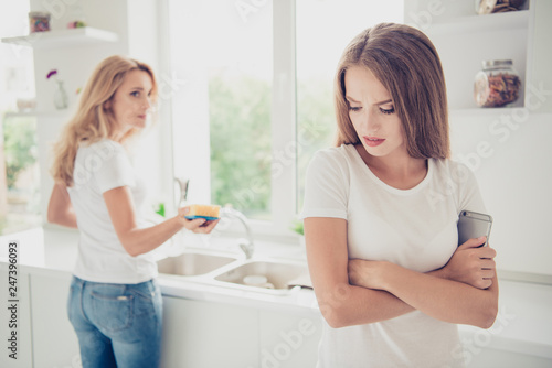 Two nice lovely attractive charming sad people blonde mom mum wiping plates kitchenware teenage girl avoiding work in modern light white interior room