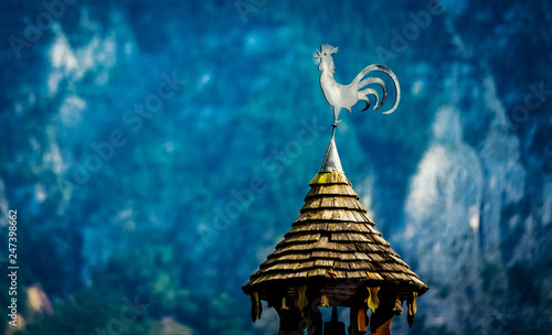 View of metal rooster on the little wooden tower roof on the mountain background photo