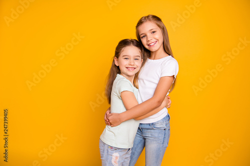 Portrait of two nice-looking cute winsome sweet attractive lovely pretty cheerful cheery positive caucasian straight-haired girls cuddling isolated over bright vivid shine yellow background