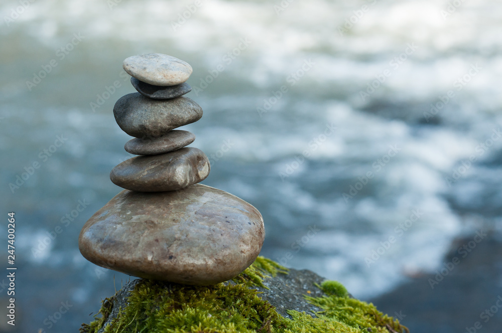Fotografie Closeup of stone balance on rock covered by moss in border river