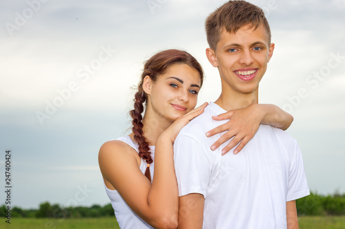 young beautiful cute couple girl and guy are standing arm in arm on a background of nature, the concept of the relationship