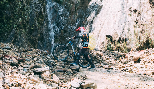 Man in special sport equipment taking a bike over stones on the background of huge mountain rocks