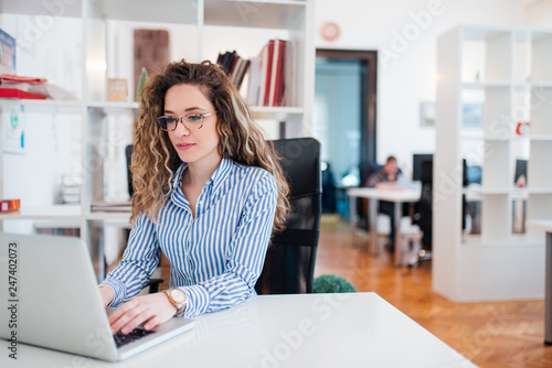 Young female accountant working on laptop in bright work station. photo