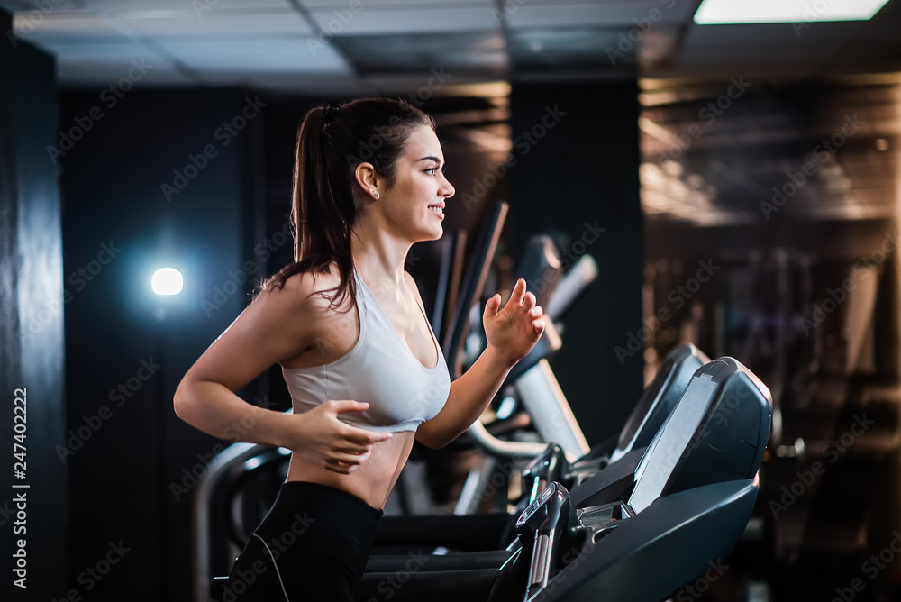 Young sports woman with ponytail working out in the gym, running on treadmill, side view. Young sports woman with ponytail working out in the gym, running on treadmill, side view.