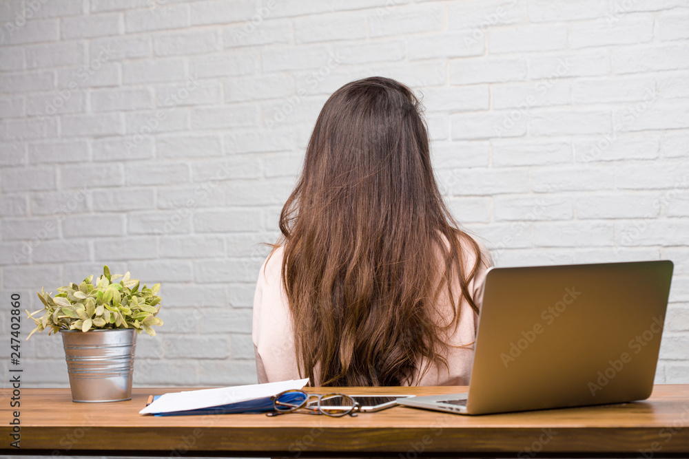 Portrait of young student latin woman sitting on her desk showing back ...