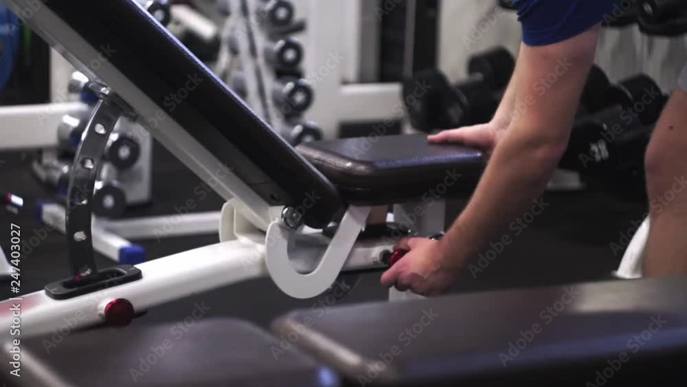 Man adjusting high of the bench before doing biceps workput in the gym Man adjusting high of the bench before doing biceps workput in the gym