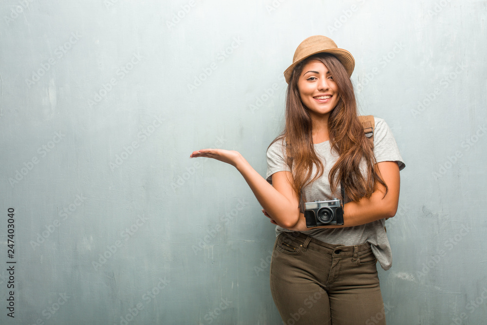 Portrait of young traveler latin woman against a wall holding something with hands, showing a product, smiling and cheerful, offering an imaginary object Portrait of young traveler latin woman against a wall holding something with hands, showing a product, smiling and cheerful, offering an imaginary object
