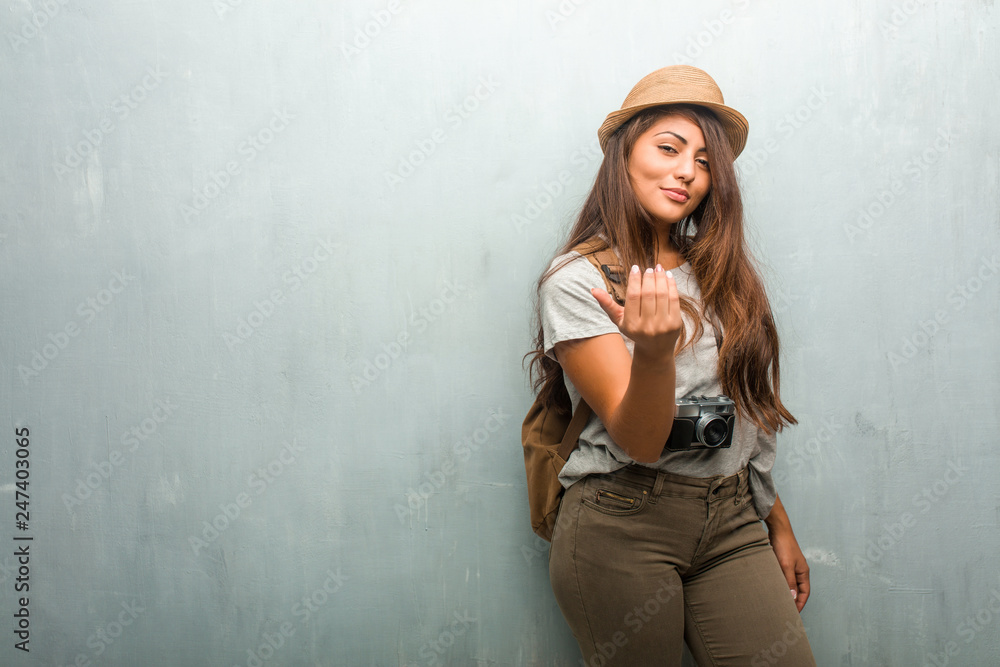 Portrait of young traveler latin woman against a wall inviting to come, confident and smiling making a gesture with hand, being positive and friendly Portrait of young traveler latin woman against a wall inviting to come, confident and smiling making a gesture with hand, being positive and friendly