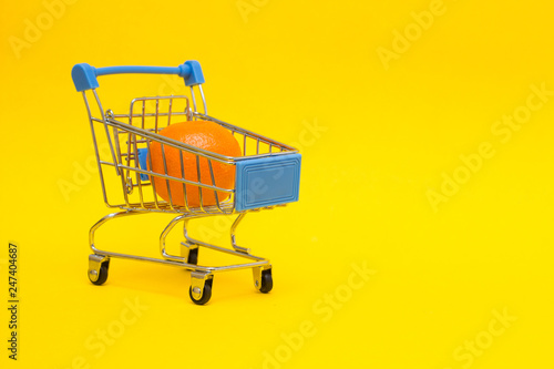 Mandarin in a shopping trolley on a yellow background, close-up, export of food and fruit abroad