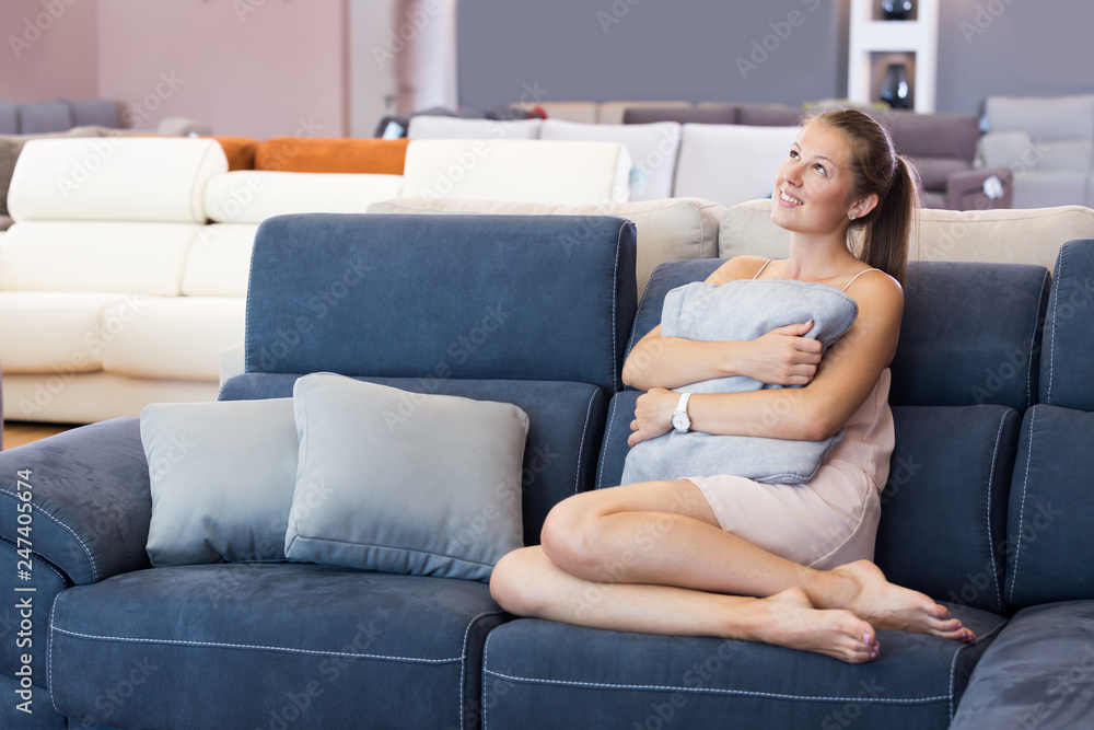 Obraz premium Glad woman sitting barefoot and testing sofa