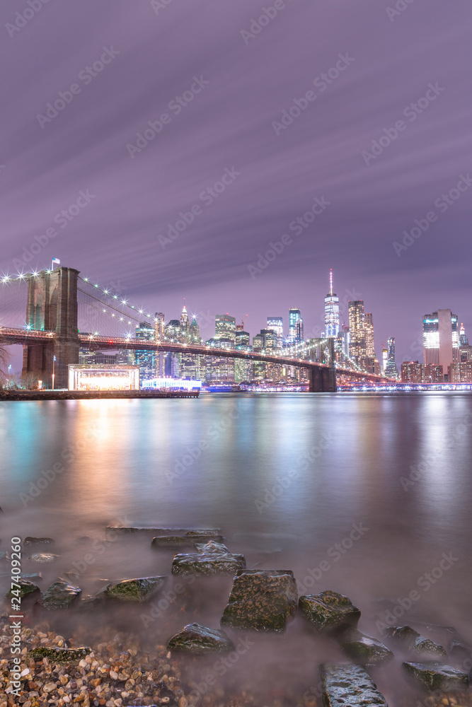 Fototapeta premium View on Financial district and Brooklyn bridge at night from East river beach with long exposure