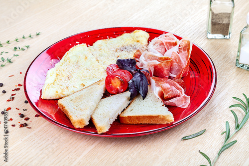 Close up view on served Italian breakfast with scrambled eggs, prosciutto, baguette, basil and cherry tomatoes. Restaurant, food menu, recipe, cafe concept. Lifestyle with copy space. Italian cuisine.