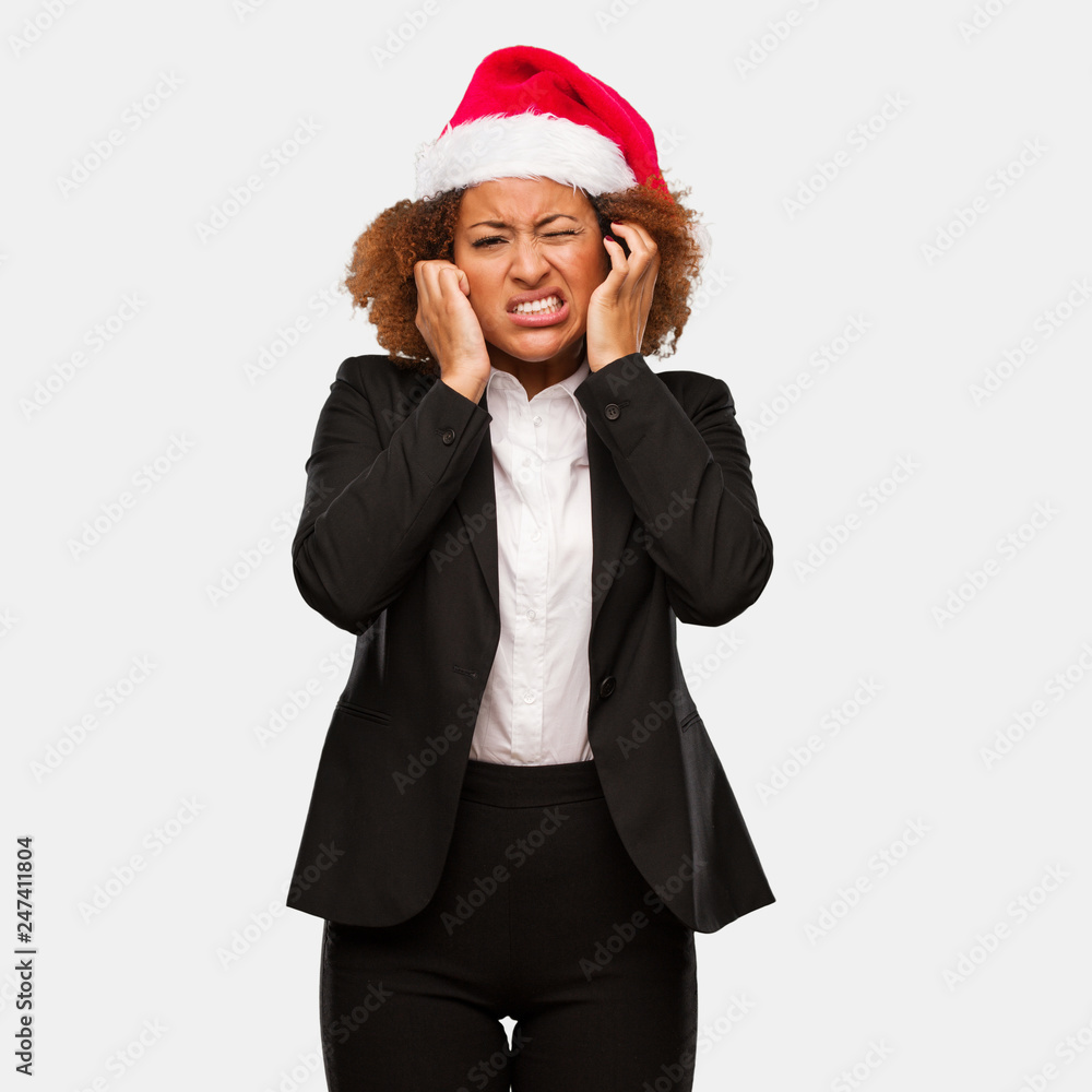 Young business black woman wearing a chirstmas santa hat covering ears with hands Young business black woman wearing a chirstmas santa hat covering ears with hands