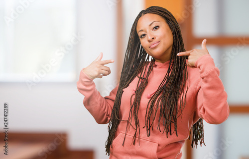 Portrait of a young black woman wearing braids proud and confident, pointing fingers, example to follow, concept of satisfaction, arrogance and health