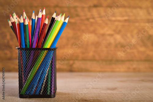 School supplies on a warm, beautiful wooden background. Colored children's pencils in a locker black holder for stationery.