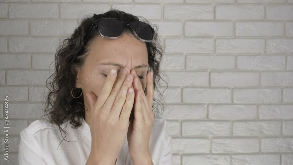Woman takes off pinhole glasses and rubbing face. The woman takes off her obscura glasses and rubs her eyes from fatigue. Woman takes off pinhole glasses and rubbing face. The woman takes off her obscura glasses and rubs her eyes from fatigue.