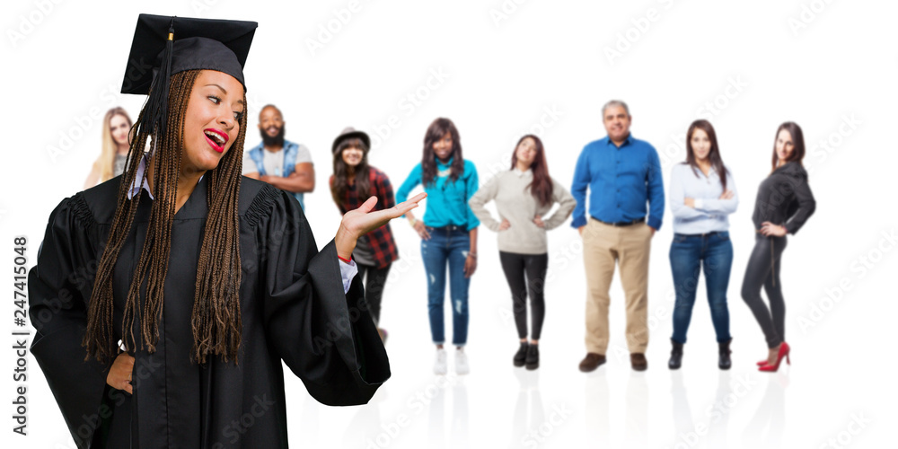 Young graduated black woman wearing braids holding something with hands, showing a product, smiling and cheerful, offering an imaginary object