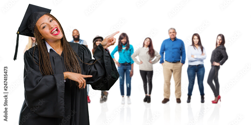 Young graduated black woman wearing braids pointing to the side, smiling surprised presenting something, natural and casual Young graduated black woman wearing braids pointing to the side, smiling surprised presenting something, natural and casual