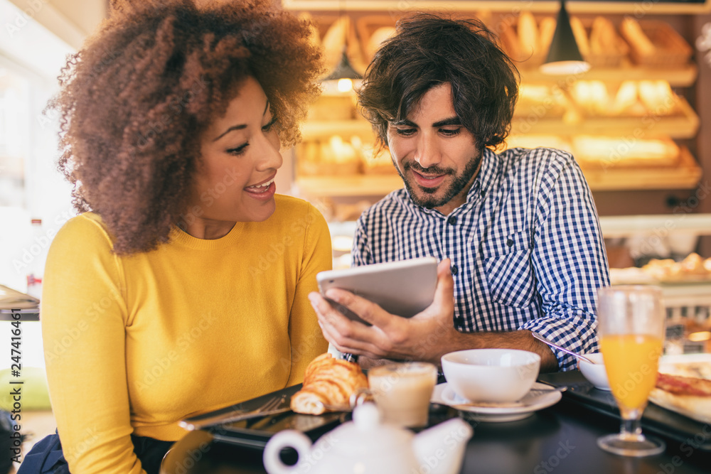 Young cool couple in a bakery, having a breakfast and using a tablet. They are having fun and smiling. Young cool couple in a bakery, having a breakfast and using a tablet. They are having fun and smiling.