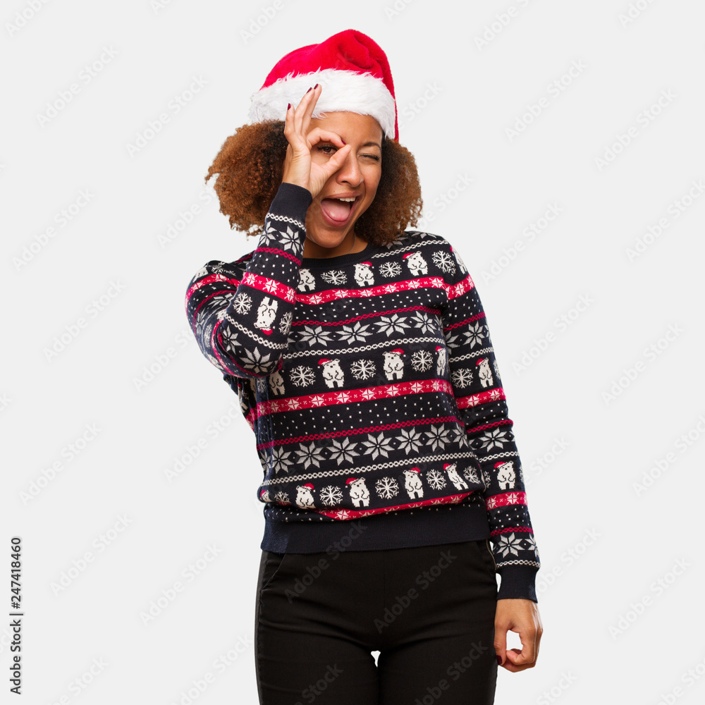 Young black woman in a trendy christmas sweater with print confident doing ok gesture on eye Young black woman in a trendy christmas sweater with print confident doing ok gesture on eye