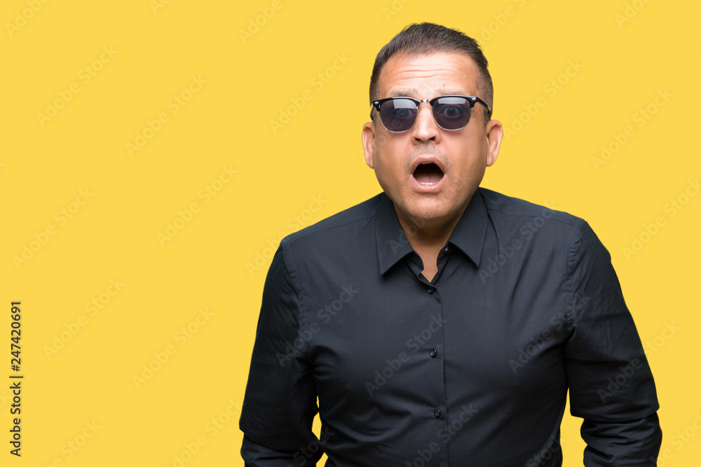 Fototapeta premium Middle age arab man wearing sunglasses over isolated background afraid and shocked with surprise expression, fear and excited face.