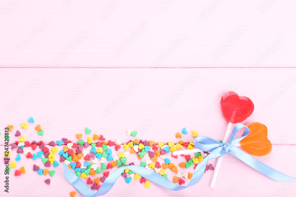 Heart shaped lollipops with colorful sprinkles and ribbon on pink wooden table