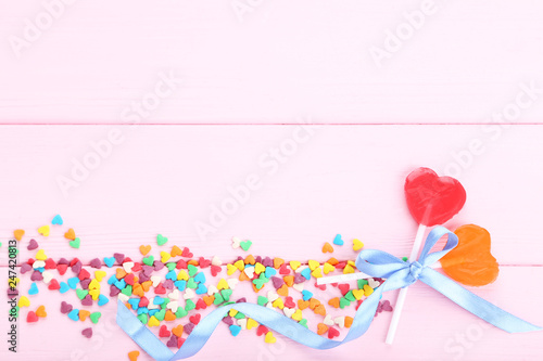 Heart shaped lollipops with colorful sprinkles and ribbon on pink wooden table