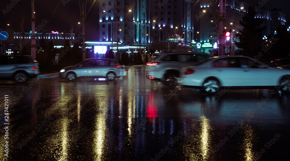 Ashgabat, Turkmenistan. Movement on a junction in rush our at 21:00. Rainy weather, city lights reflected on a surface (asphalt) Out of focus, motion blur.