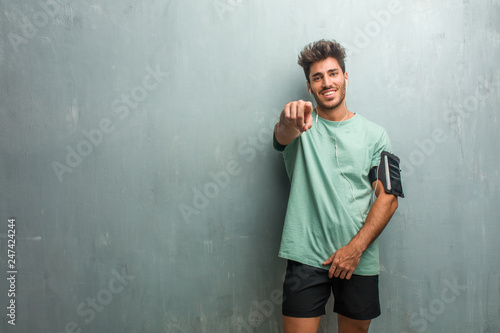 Young fitness man against a grunge wall shouting, laughing and making fun of another, concept of mockery and uncontrol. Wearing an armband with phone.