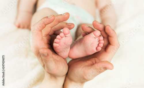 hand holding newborn baby feet in hear shape. Macro photo of adorable little boy toes with plush lining cozy blanket background