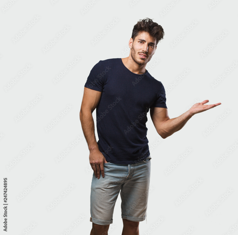 Young handsome man standing holding something with hands, showing a product, smiling and cheerful, offering an imaginary object Young handsome man standing holding something with hands, showing a product, smiling and cheerful, offering an imaginary object
