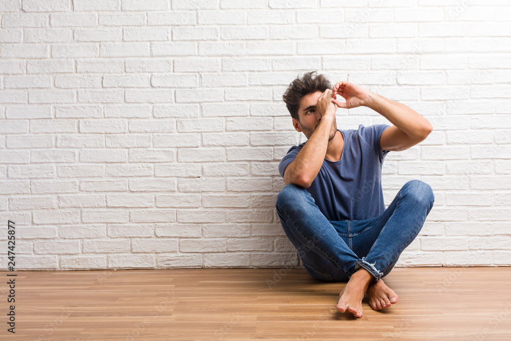 Young natural man sit on a wooden floor looking through a gap, hiding and squinting Young natural man sit on a wooden floor looking through a gap, hiding and squinting