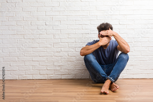 Young natural man sit on a wooden floor looking through a gap, hiding and squinting