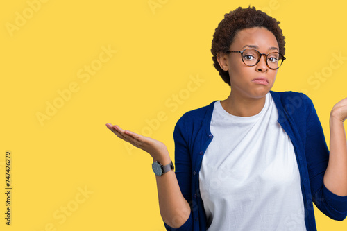 Young beautiful african american woman wearing glasses over isolated background clueless and confused expression with arms and hands raised. Doubt concept.