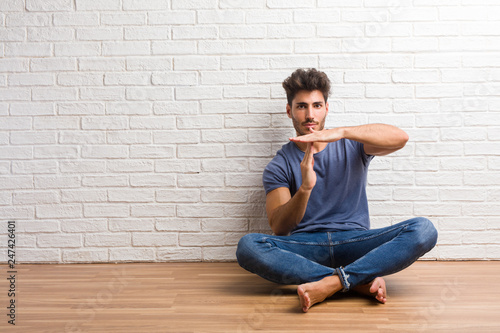 Young natural man sit on a wooden floor tired and bored, making a timeout gesture, needs to stop because of work stress, time concept