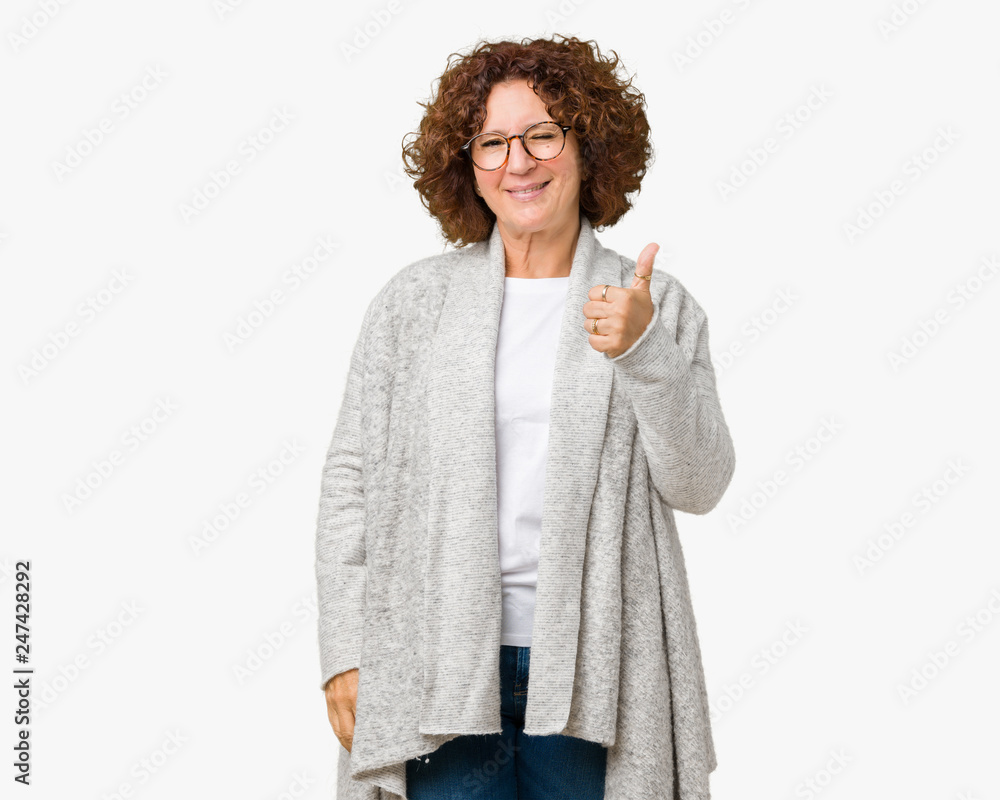 Beautiful middle ager senior woman wearing jacket and glasses over isolated background doing happy thumbs up gesture with hand. Approving expression looking at the camera showing success. Beautiful middle ager senior woman wearing jacket and glasses over isolated background doing happy thumbs up gesture with hand. Approving expression looking at the camera showing success.