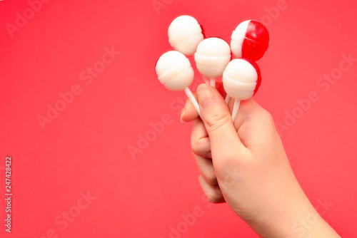 Lollipop in female hand on red background. Space for text or design.