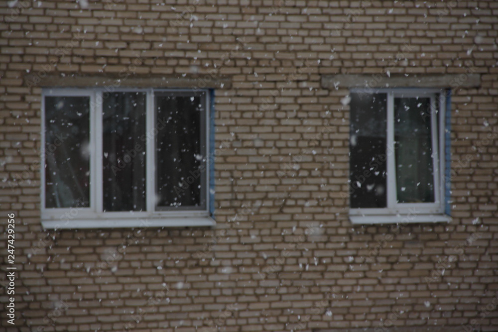 The wall of an old brick house on the background of snowfall - heating, preparation for winter, installation of plastic Windows