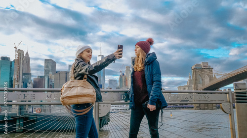 Two young women in New York walk along the typical skyline at Brooklyn Bridge