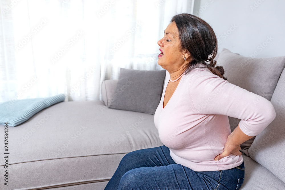 Upset mature middle aged woman feels back pain massaging aching muscles, sad senior older lady suffers from low-back lumbar pain sitting in incorrect sedentary posture, backache radiculitis concept Upset mature middle aged woman feels back pain massaging aching muscles, sad senior older lady suffers from low-back lumbar pain sitting in incorrect sedentary posture, backache radiculitis concept
