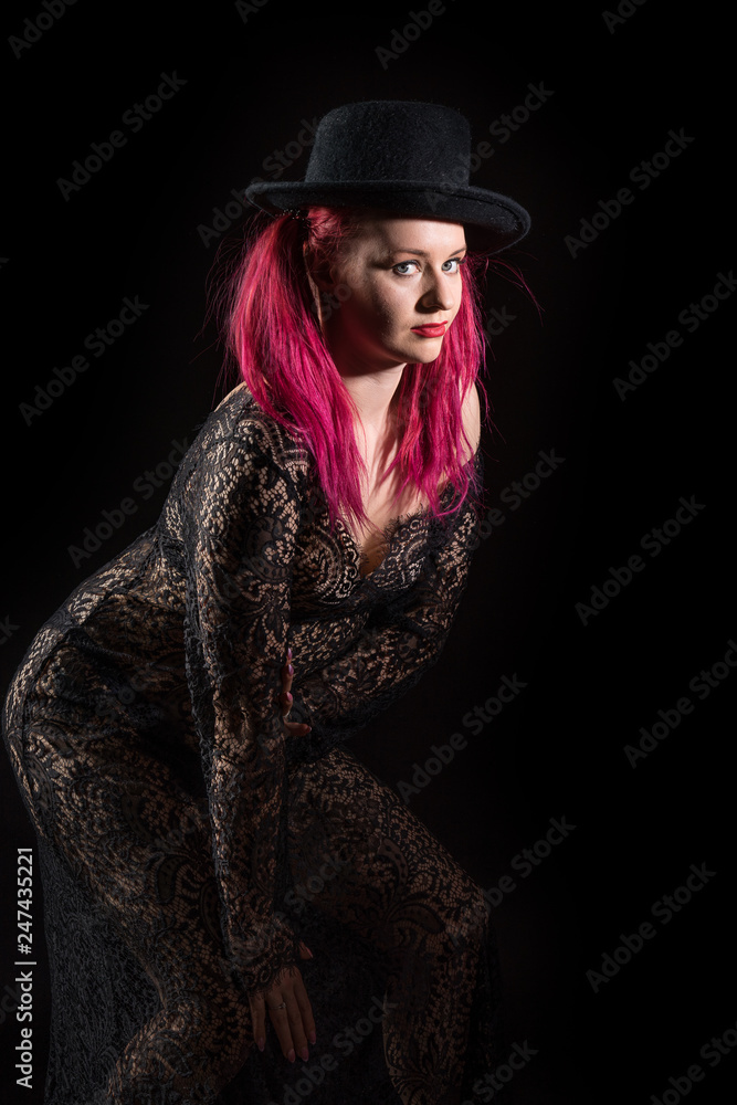 Beautiful woman with red long hair wearing a lacy dress and hat. Beauty portrait of modern fashion, black background.