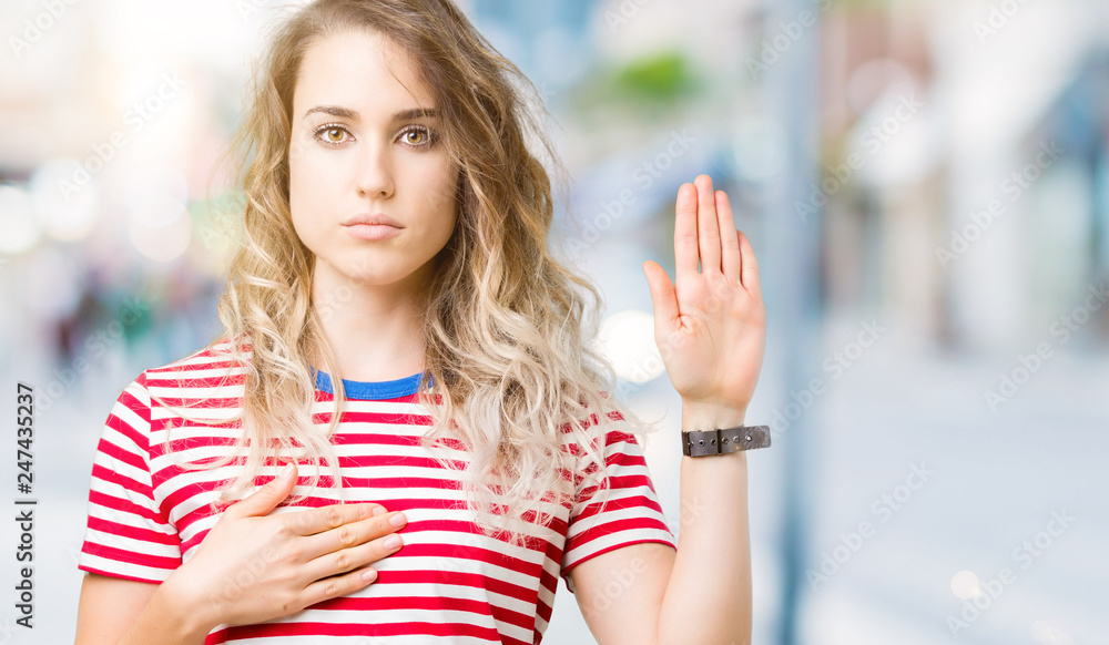 Beautiful young blonde woman over isolated background Swearing with hand on chest and open palm, making a loyalty promise oath