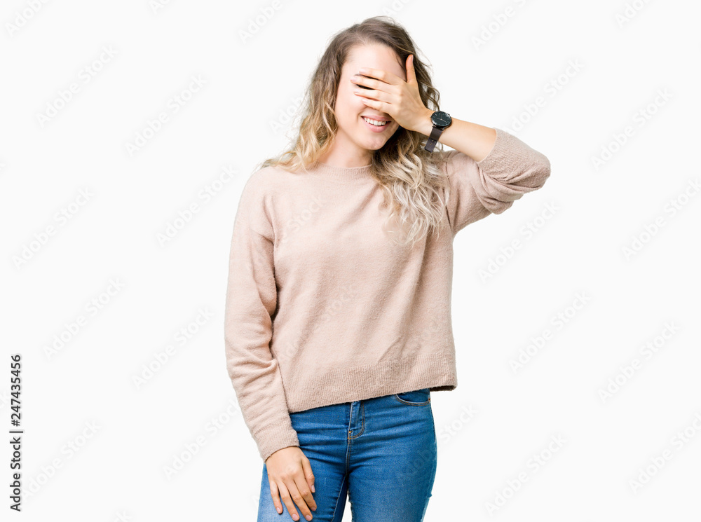Beautiful young blonde woman wearing sweatershirt over isolated background smiling and laughing with hand on face covering eyes for surprise. Blind concept. Beautiful young blonde woman wearing sweatershirt over isolated background smiling and laughing with hand on face covering eyes for surprise. Blind concept.