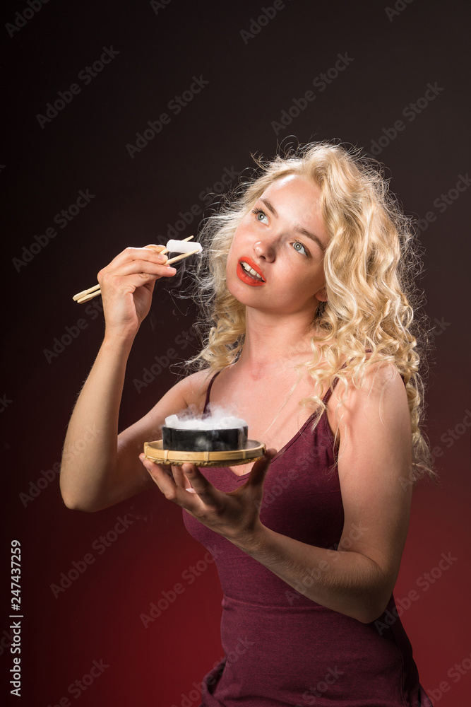 Beautiful woman with blonde long curly hair holds chopsticks and eats. Beauty portrait of modern fashion, red background. Beautiful woman with blonde long curly hair holds chopsticks and eats. Beauty portrait of modern fashion, red background.